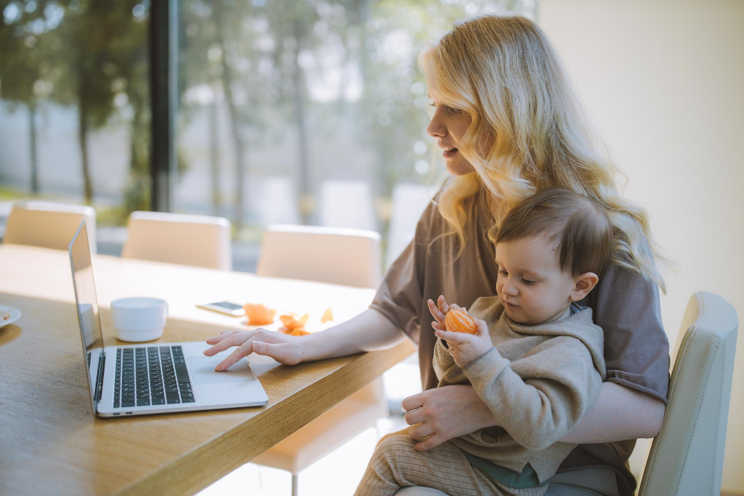 Image of a working parent, using the computer while holding a child.