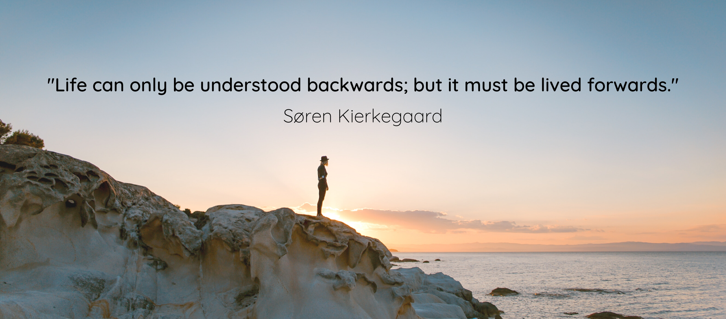 Quote overlayed on picture of a person at the costline watching the sunset over a rocky cliff. Soren Kierkegaard - "Life can only be understood backwards; but must be lived forwards"
