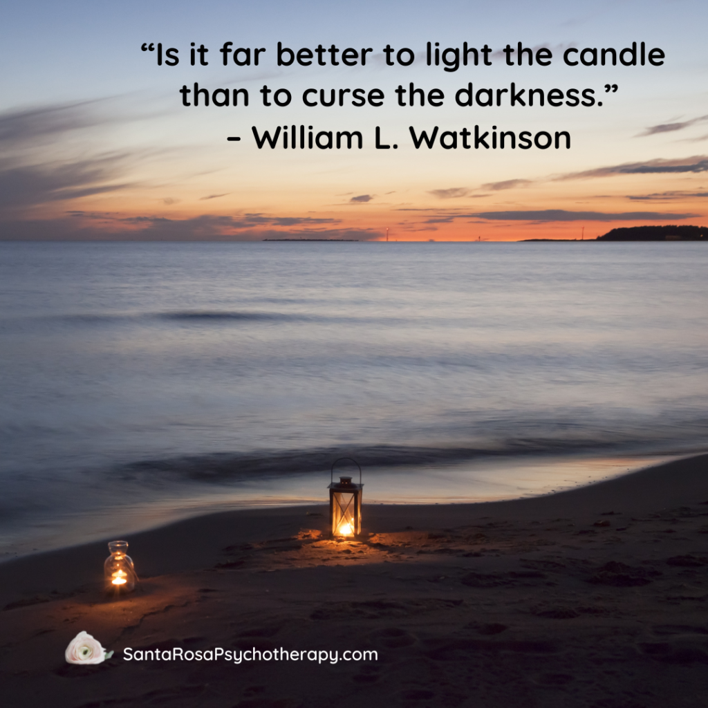 Picture of the sunset on a beach with small glowing lanterns lit, featuring the quote “Is it far better to light the candle than to curse the darkness.” – William L. Watkinson